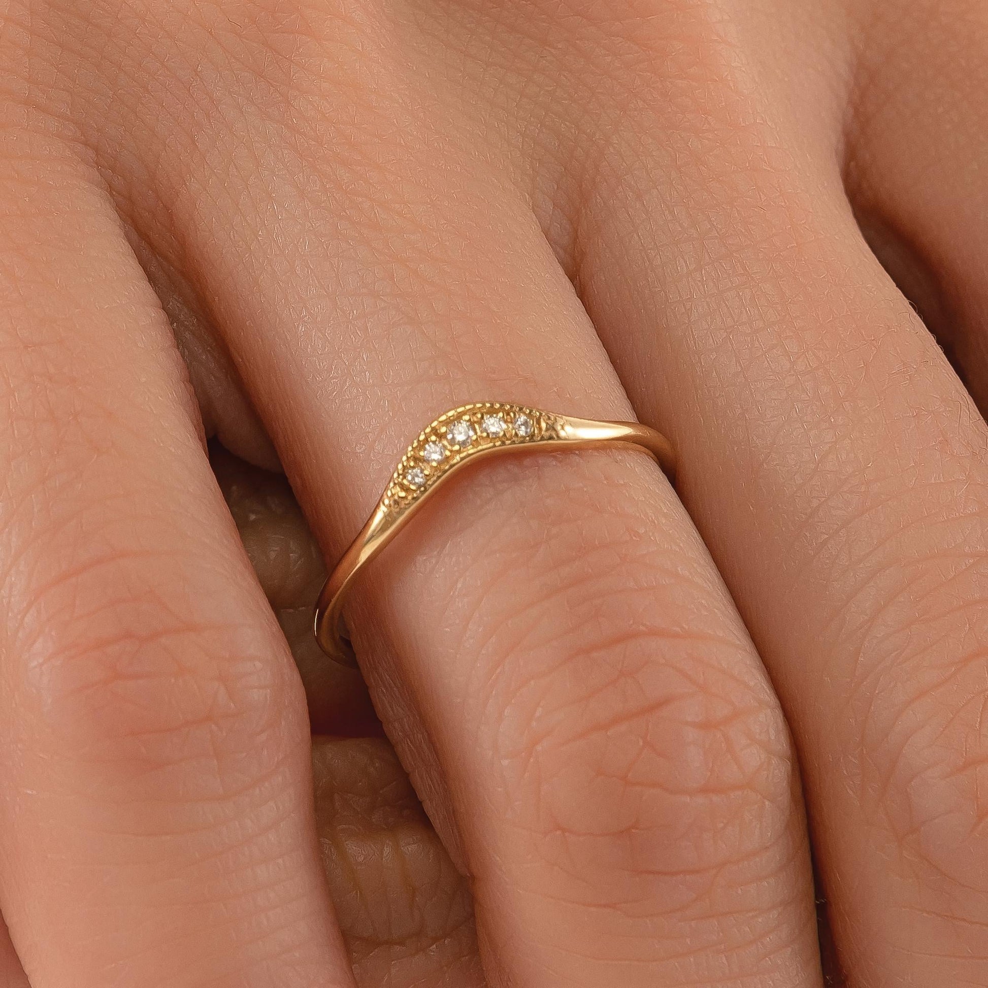 A close-up of a gold ring with a diamond-encrusted band on a person's hand.