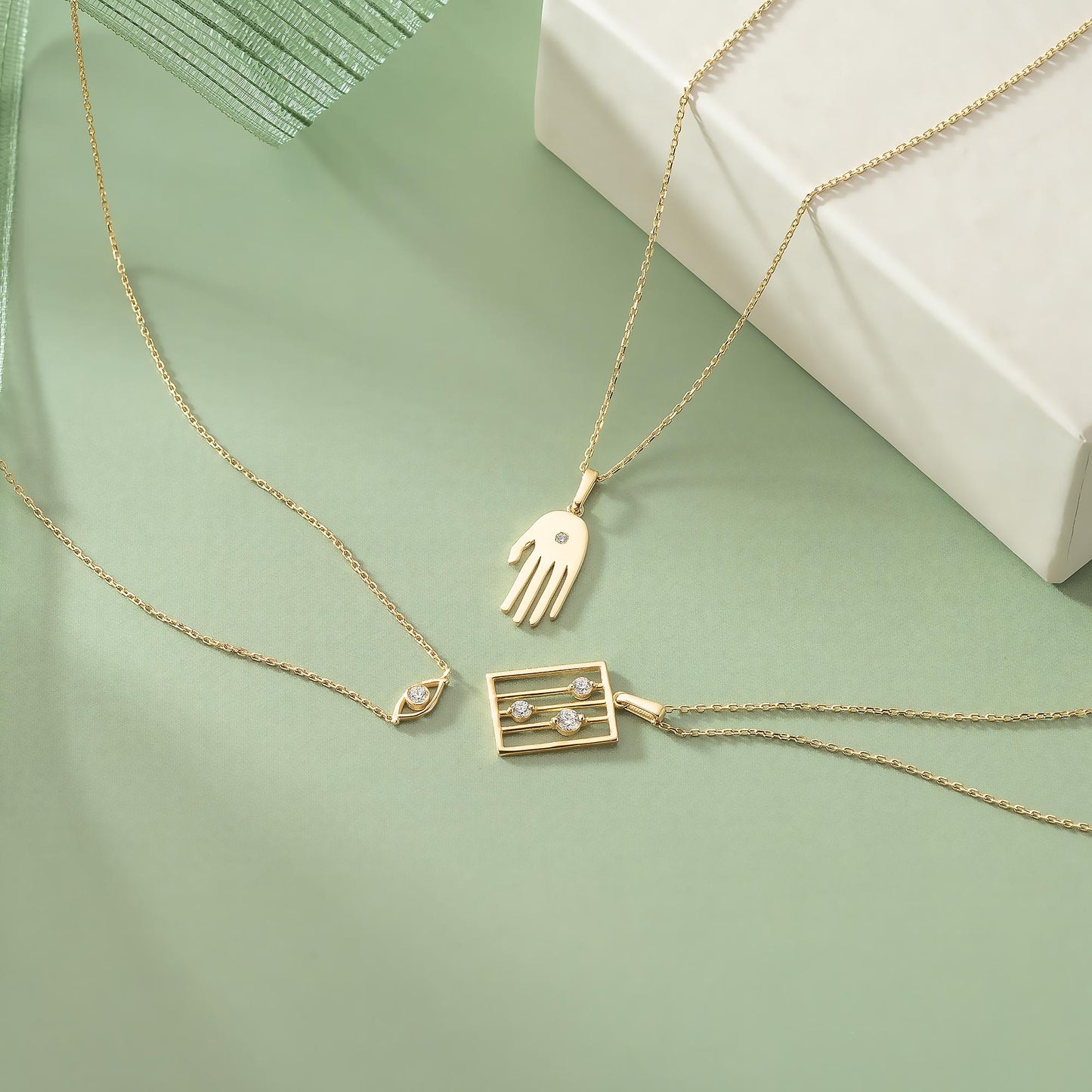 a collection of three gold necklaces with various pendants, including a heart-shaped pendant, a rectangular pendant with a small square design, and a round pendant. The necklaces are arranged on a green background, creating a visually appealing and elegant display.