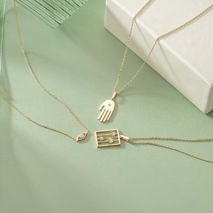 a collection of three gold necklaces with various pendants, including a heart-shaped pendant, a rectangular pendant with a small square design, and a round pendant. The necklaces are arranged on a green background, creating a visually appealing and elegant display.