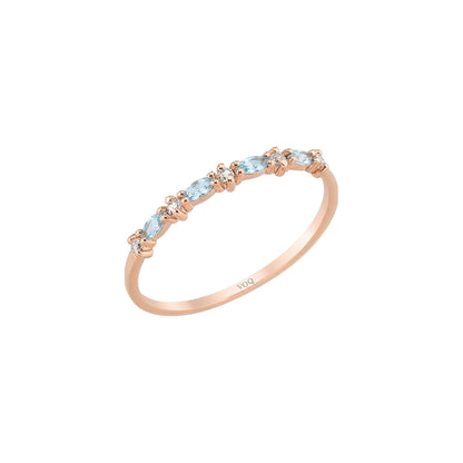 A rose gold ring with a row of aquamarine marquise and round moissanite stones on the band.
