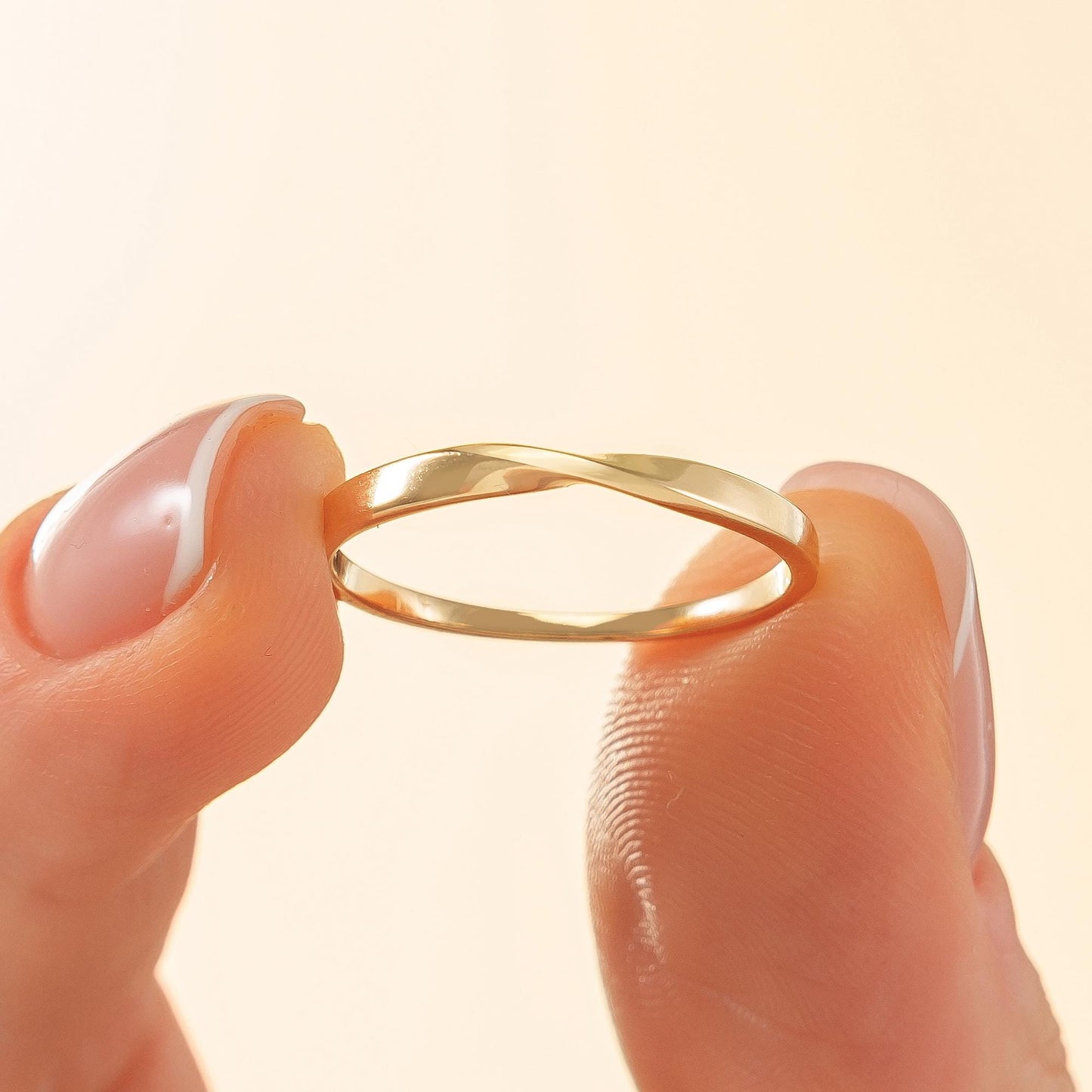 A gold ring is being held between two fingers, with the ring's design and the fingers' position visible.