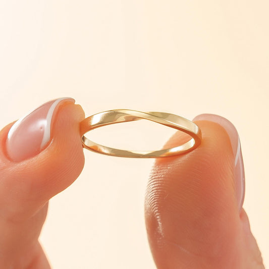 A gold ring is being held between two fingers, with the ring's design and the fingers' position visible.