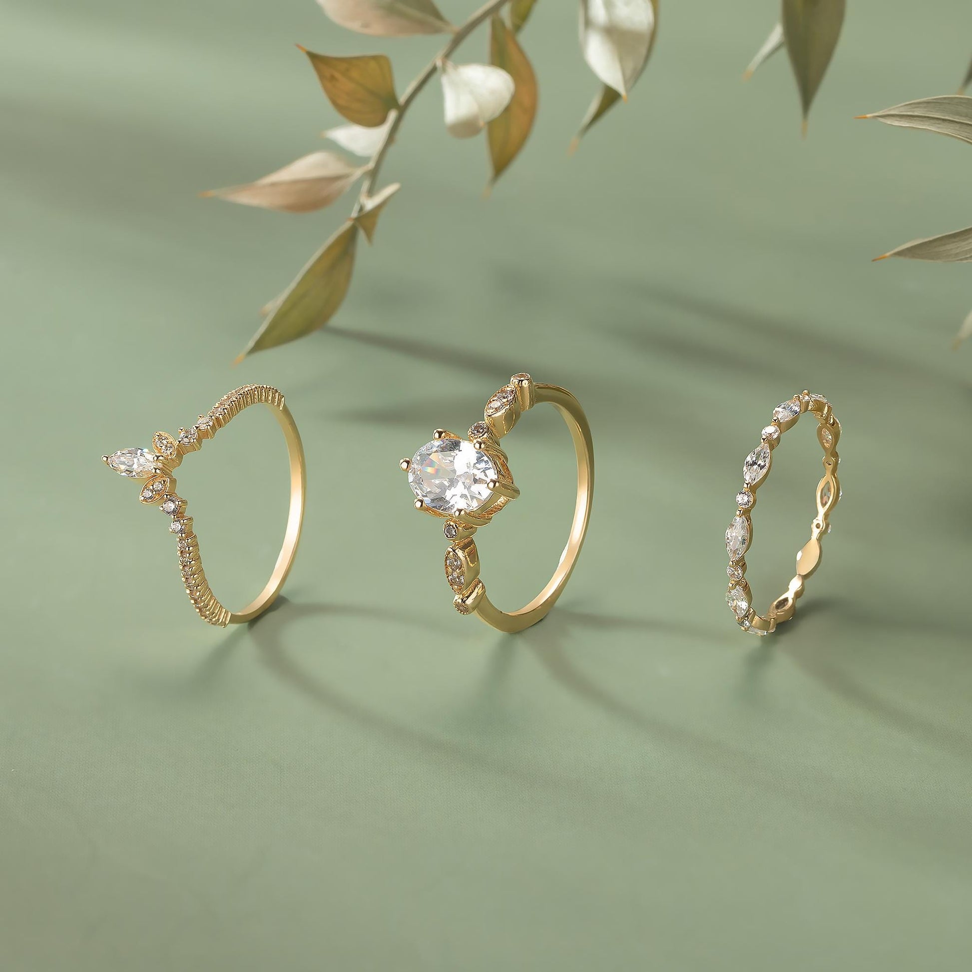 Three gold rings with various designs and gemstones are displayed on a green background.
