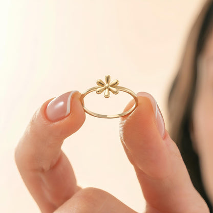 A person's hand holding a gold ring with a flower design.