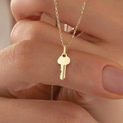A person's hand holding a small gold-colored key charm necklace.