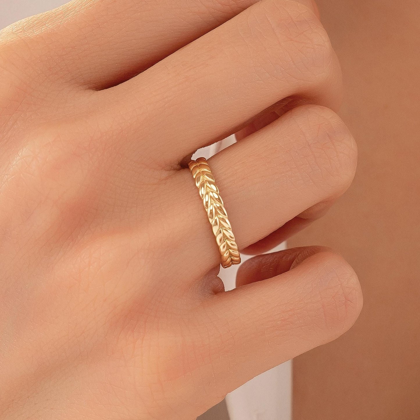 A close-up of a person's hand wearing a gold ring with a leaf-like design.