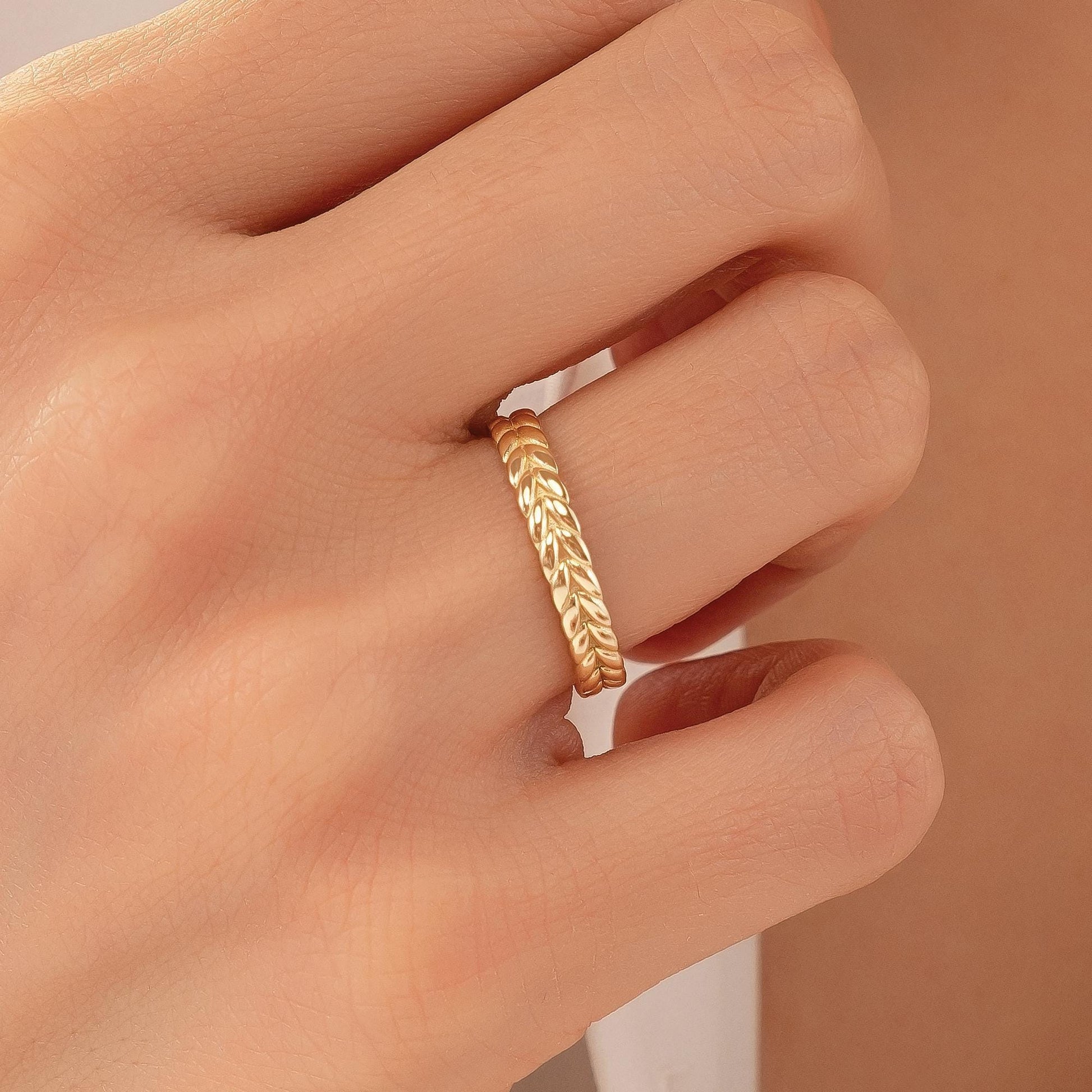 A close-up of a person's hand wearing a gold ring with a leaf-like design.