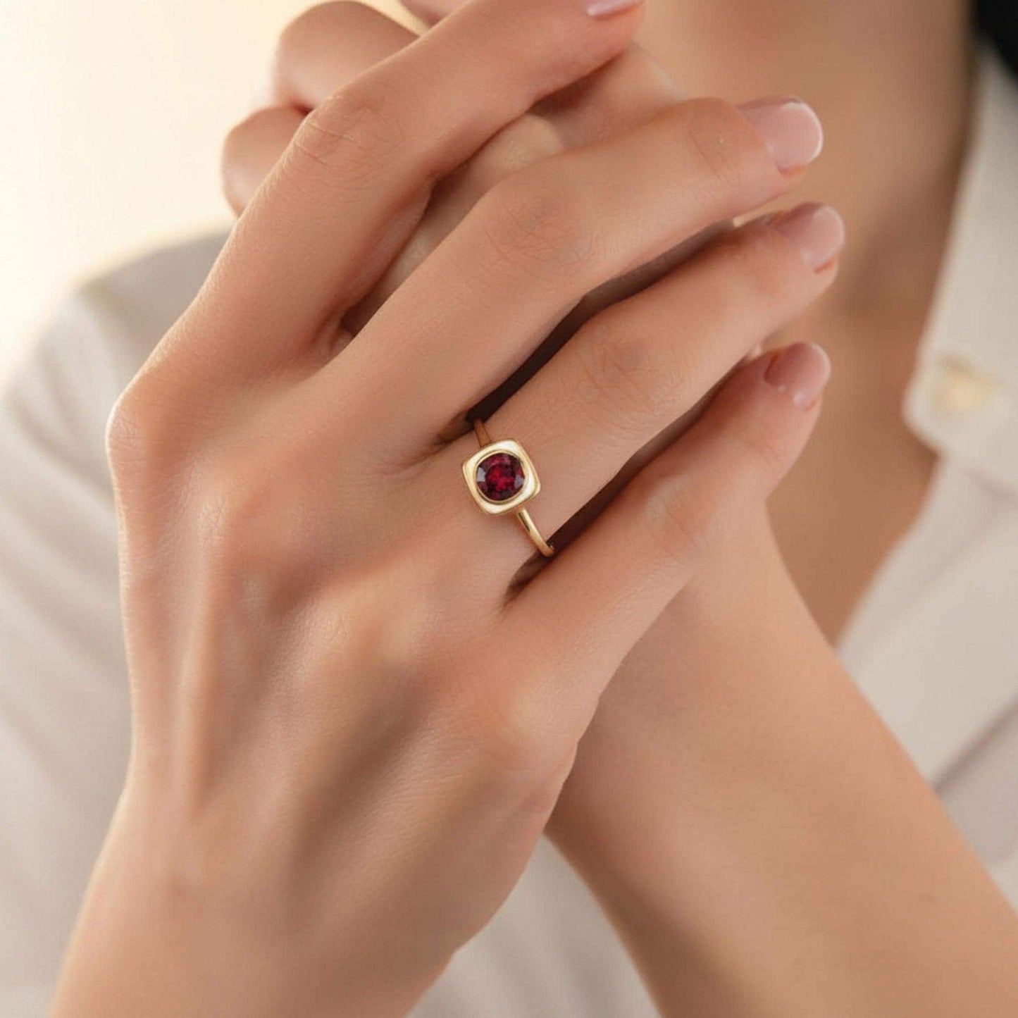 A close-up of a person's hands wearing a gold ring with a red gemstone, possibly a garnet.