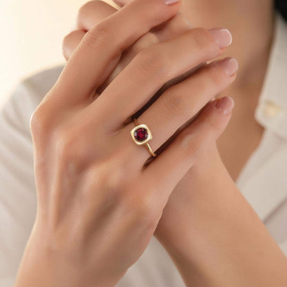 A close-up of a person's hands wearing a gold ring with a red gemstone, possibly a garnet.