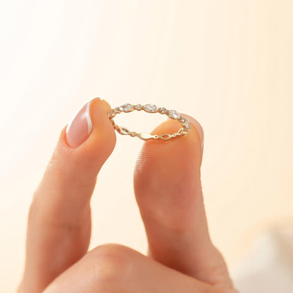 A person's hand holding a delicate gold ring with a row of small diamonds set in it.