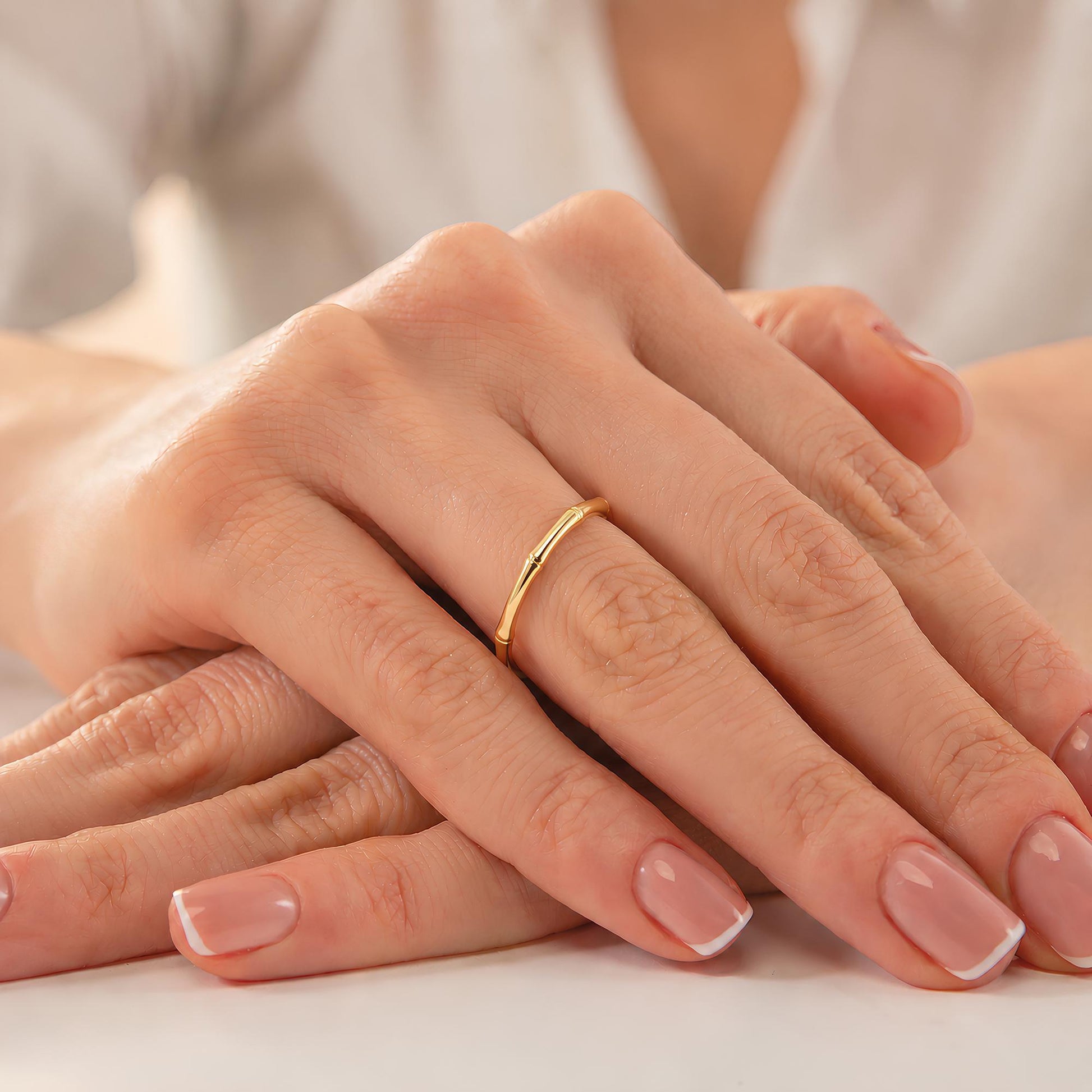 A close-up image of a person's hands with a gold ring on the ring finger.