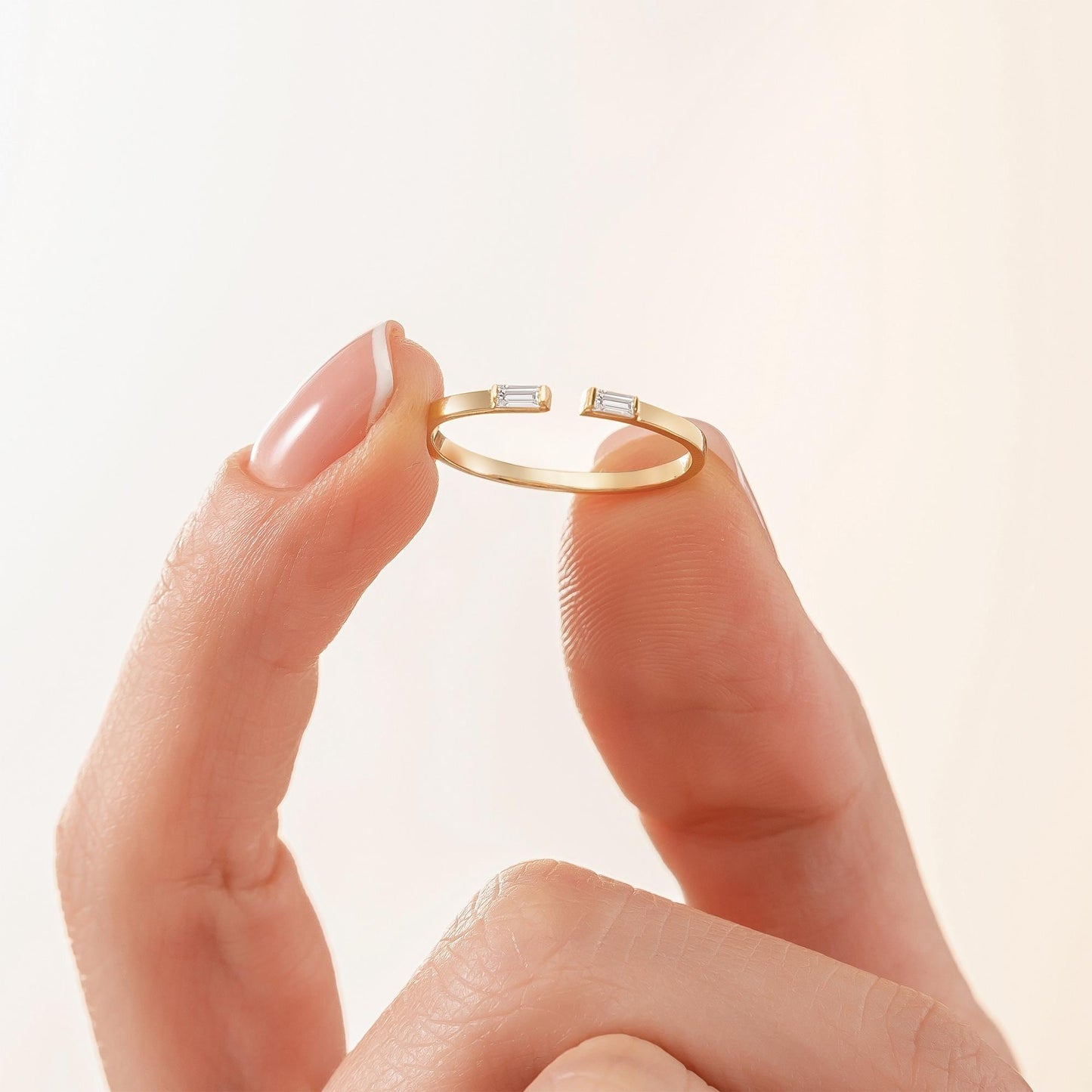 A close-up image of a person's hand holding a gold ring with two small diamonds.