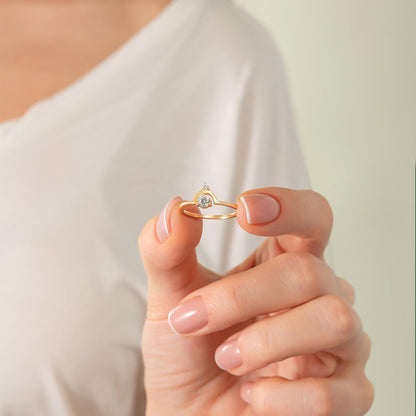 A person's hand holding a gold ring with a small diamond in the center.