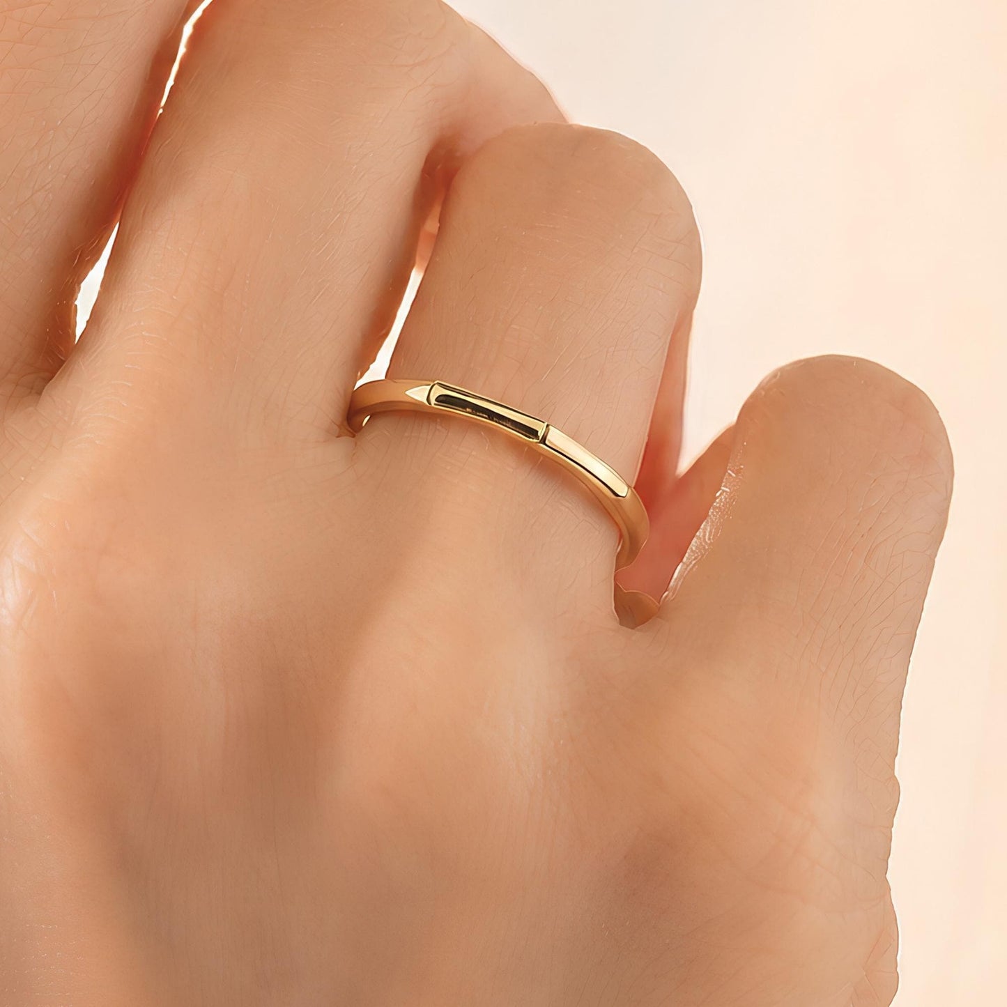 A close-up of a person's hand wearing a gold ring on the ring finger.