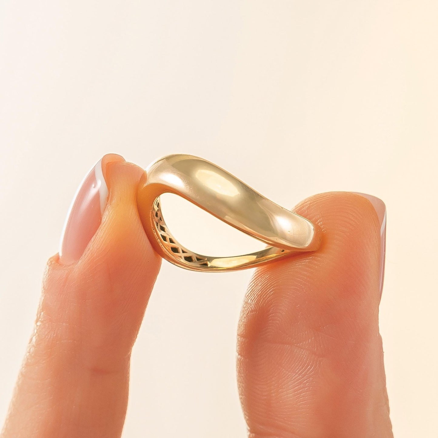 A close-up image of a person's fingers holding a gold ring with a unique, curved design.