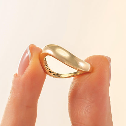 A close-up image of a person's fingers holding a gold ring with a unique, curved design.