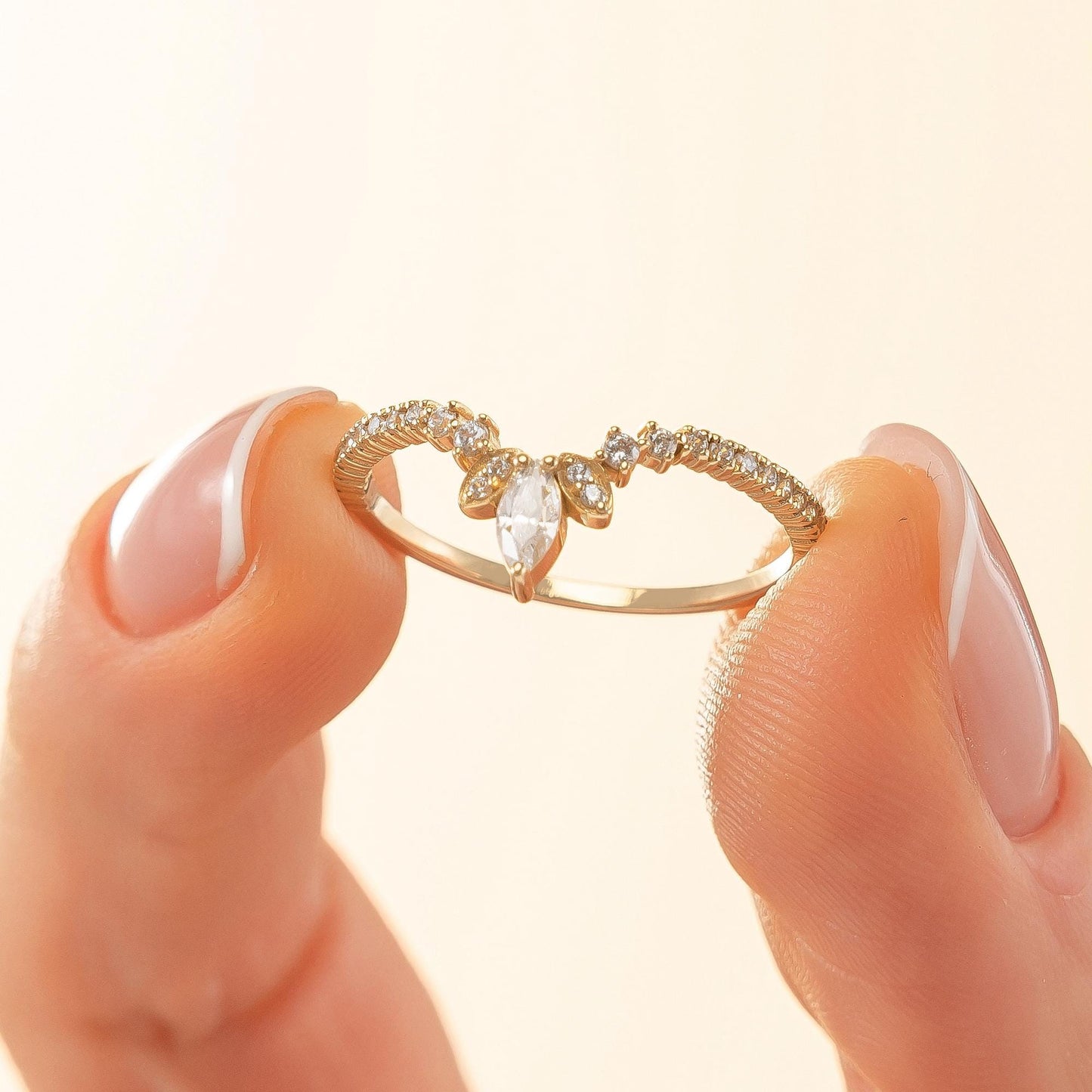 A close-up image of a person's fingers holding a gold ring with a large central stone.