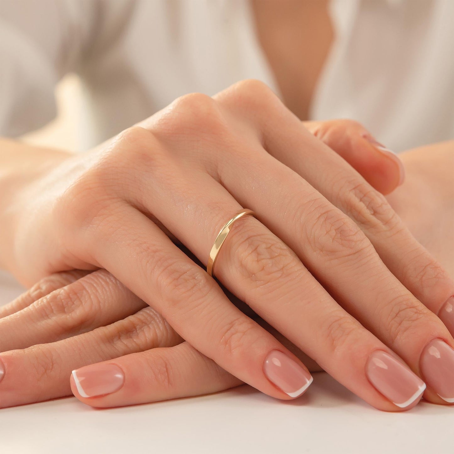 A close-up image of a person's hands with a gold ring on the ring finger.