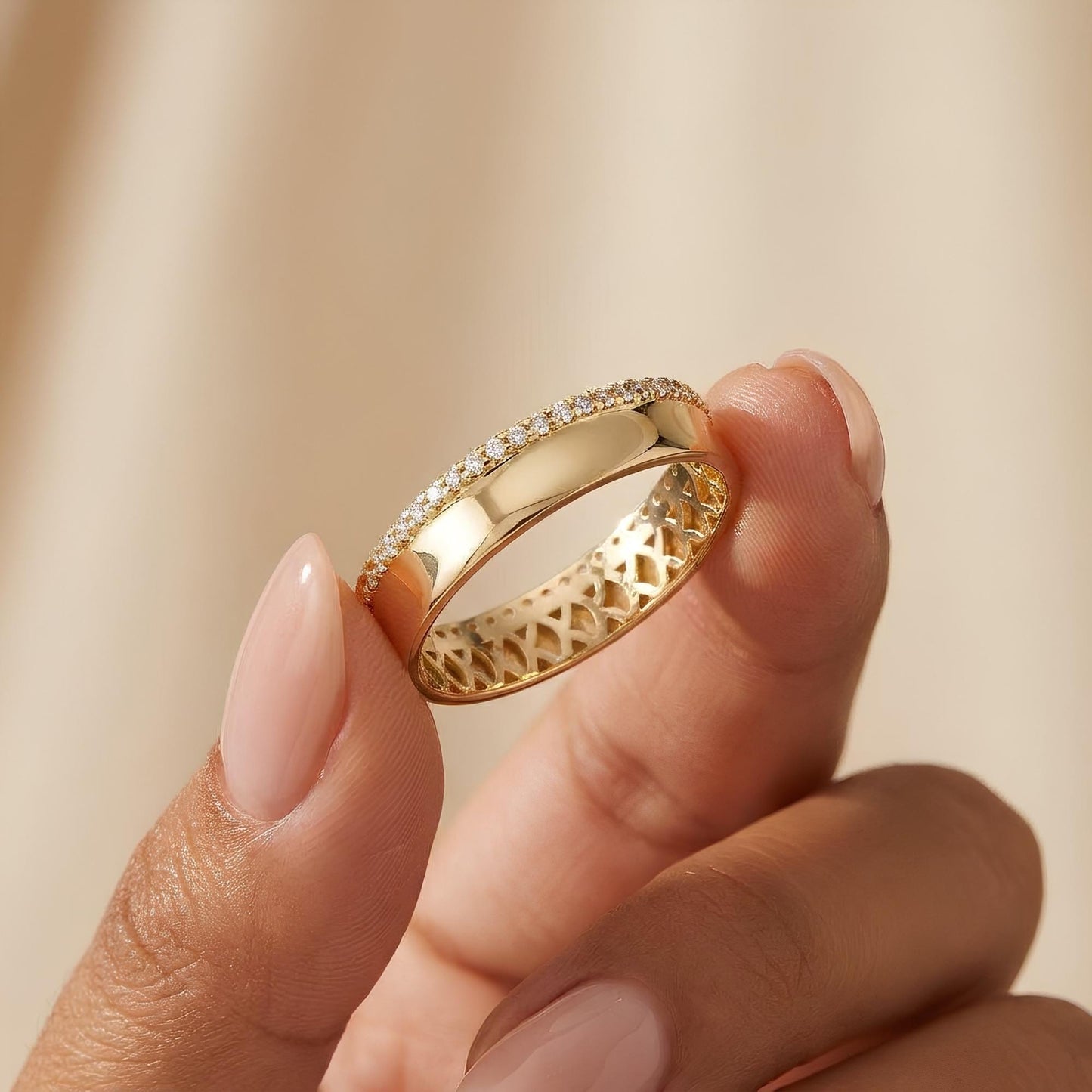 A close-up image of a person's hand holding a gold ring with a diamond accent.