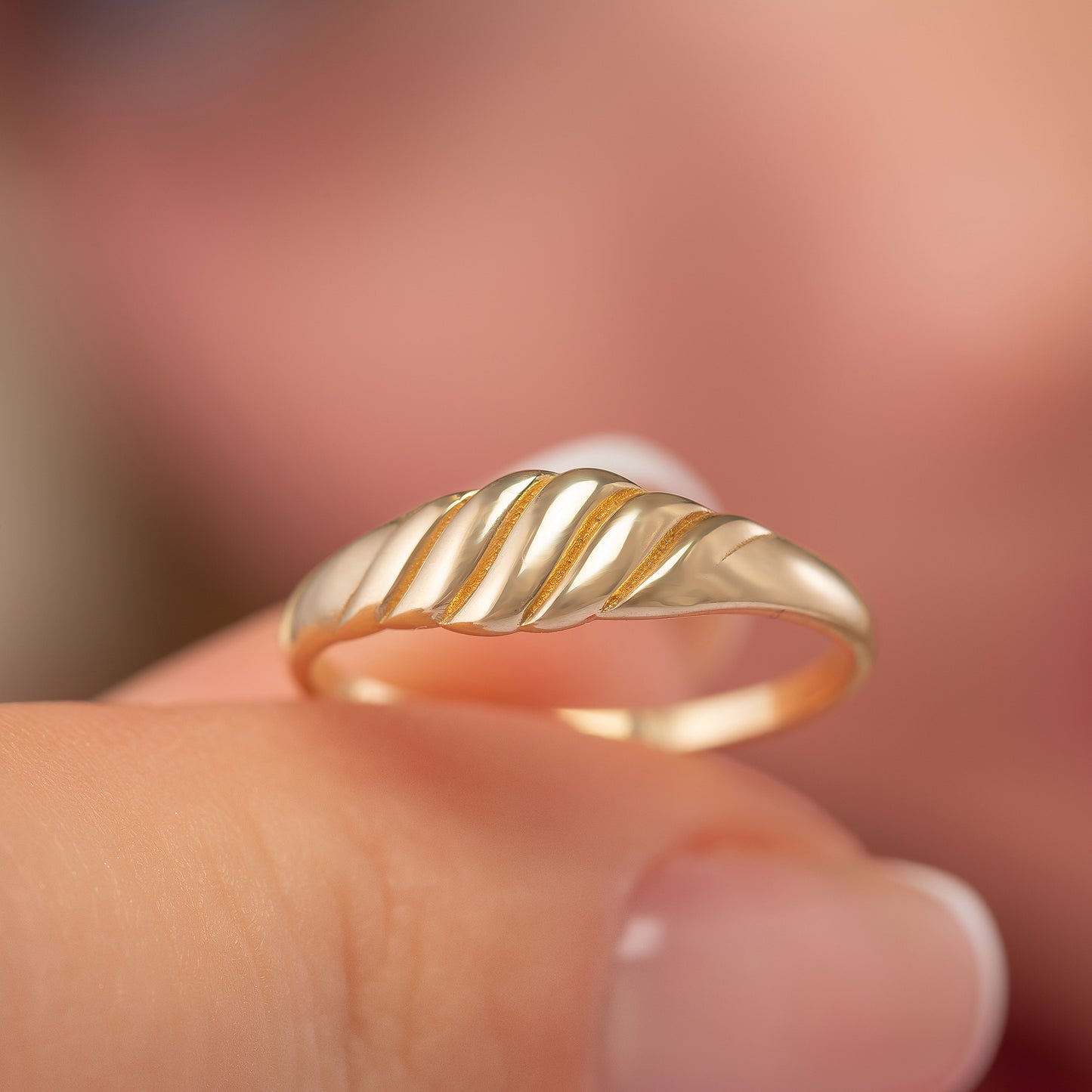 A close-up image of a person's hand wearing a gold ring with a decorative band.