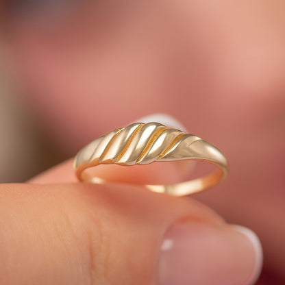 A close-up image of a person's hand wearing a gold ring with a decorative band.