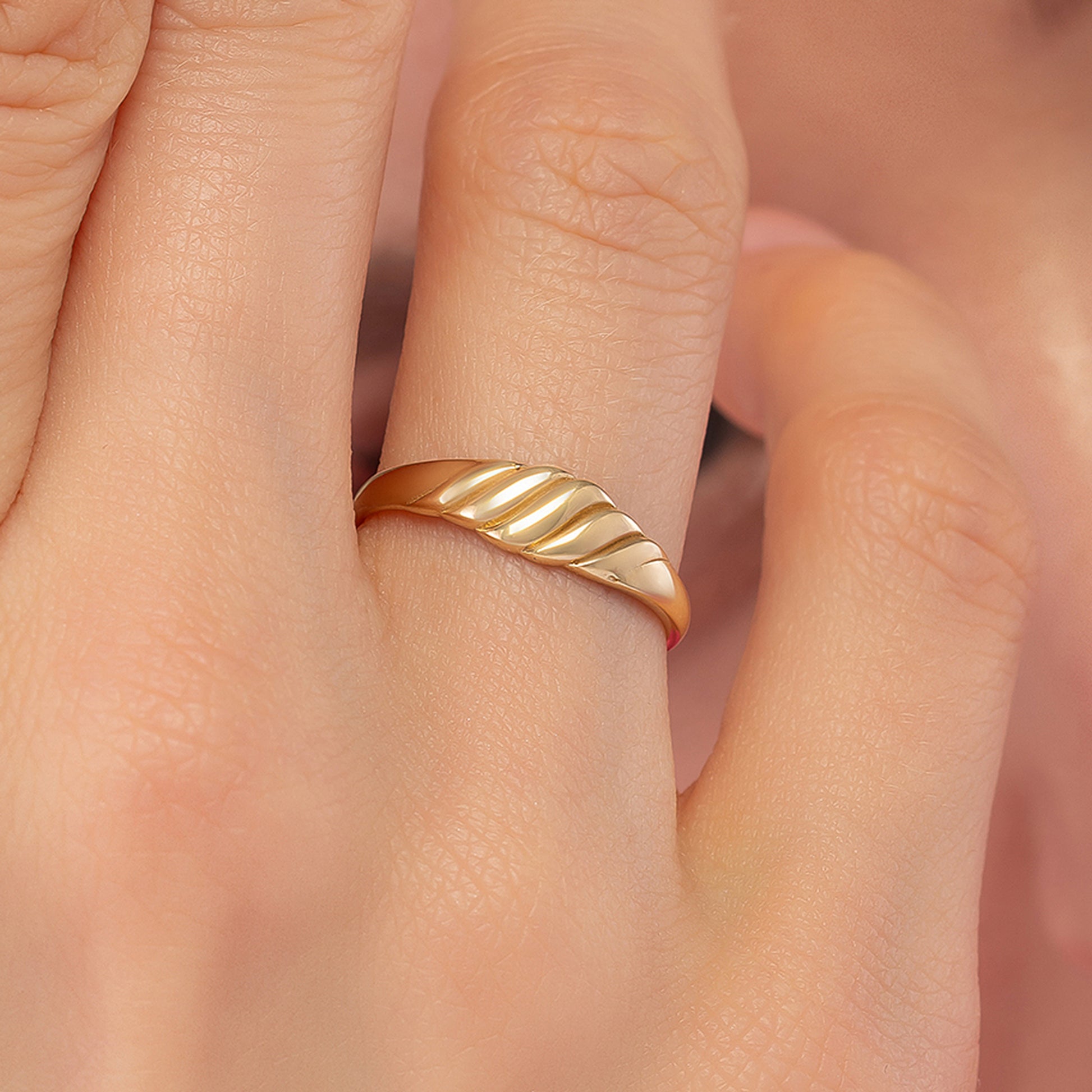 A close-up of a person's hand wearing a gold ring with a unique, curved design.
