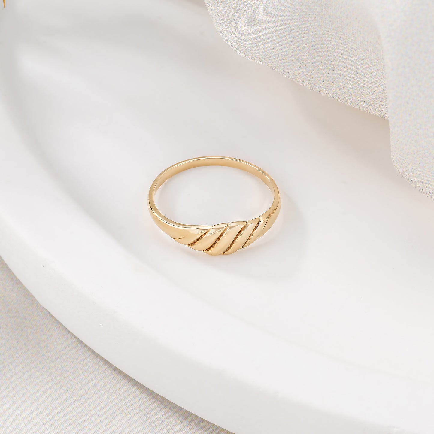 A gold ring with a curved band is displayed on a white surface.