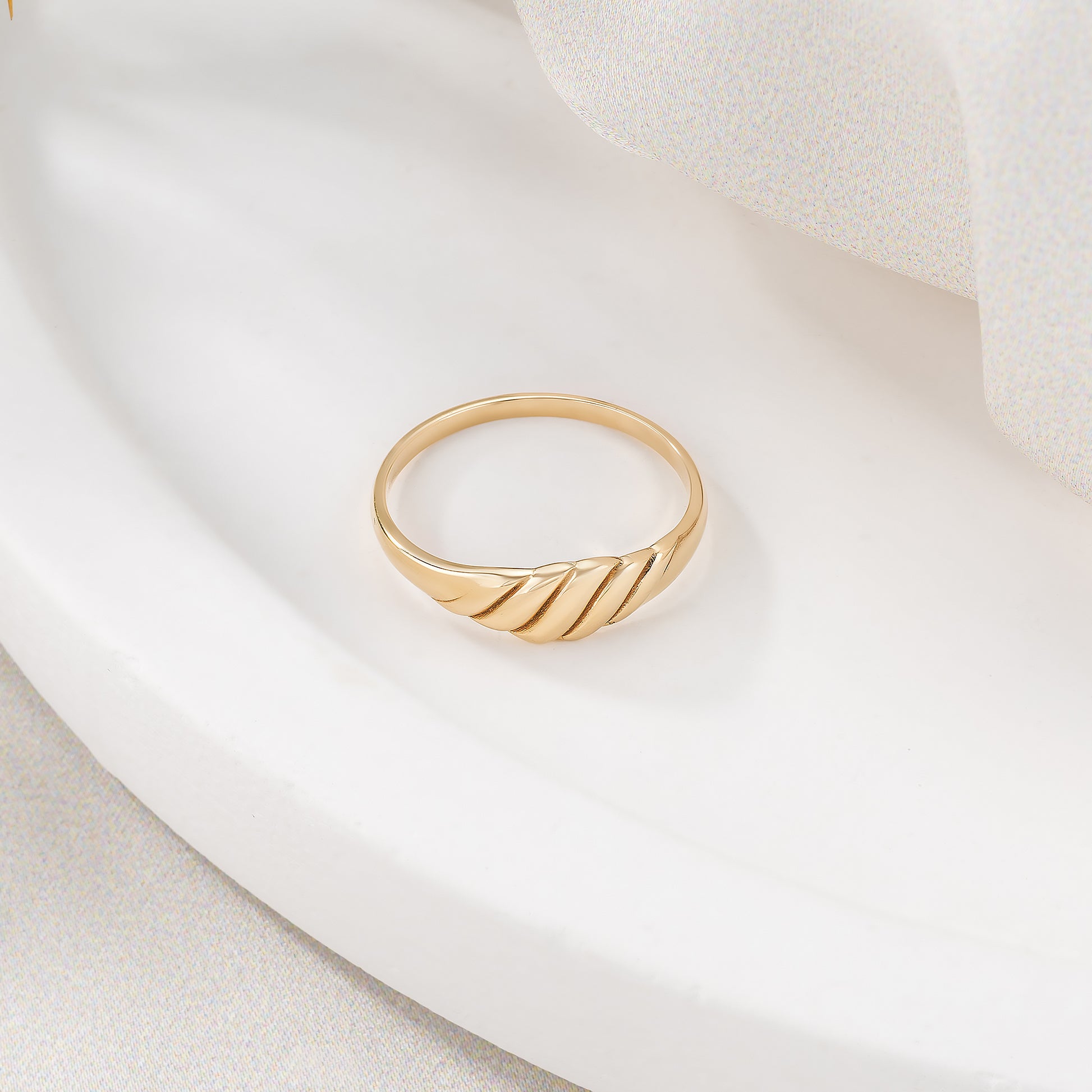 A gold ring with a curved band is displayed on a white surface.