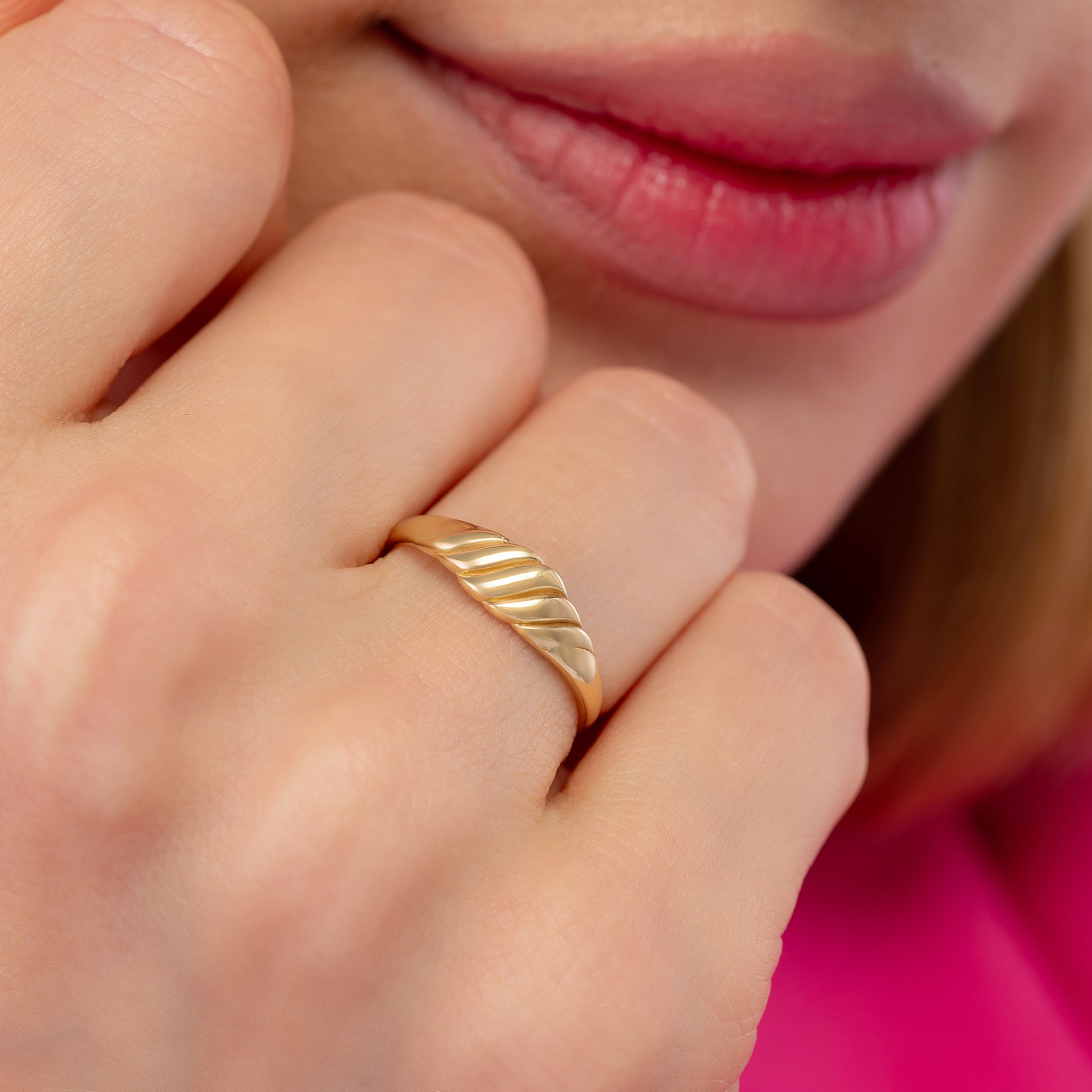 A close-up of a person's hand wearing a gold ring, with their lips visible in the background.