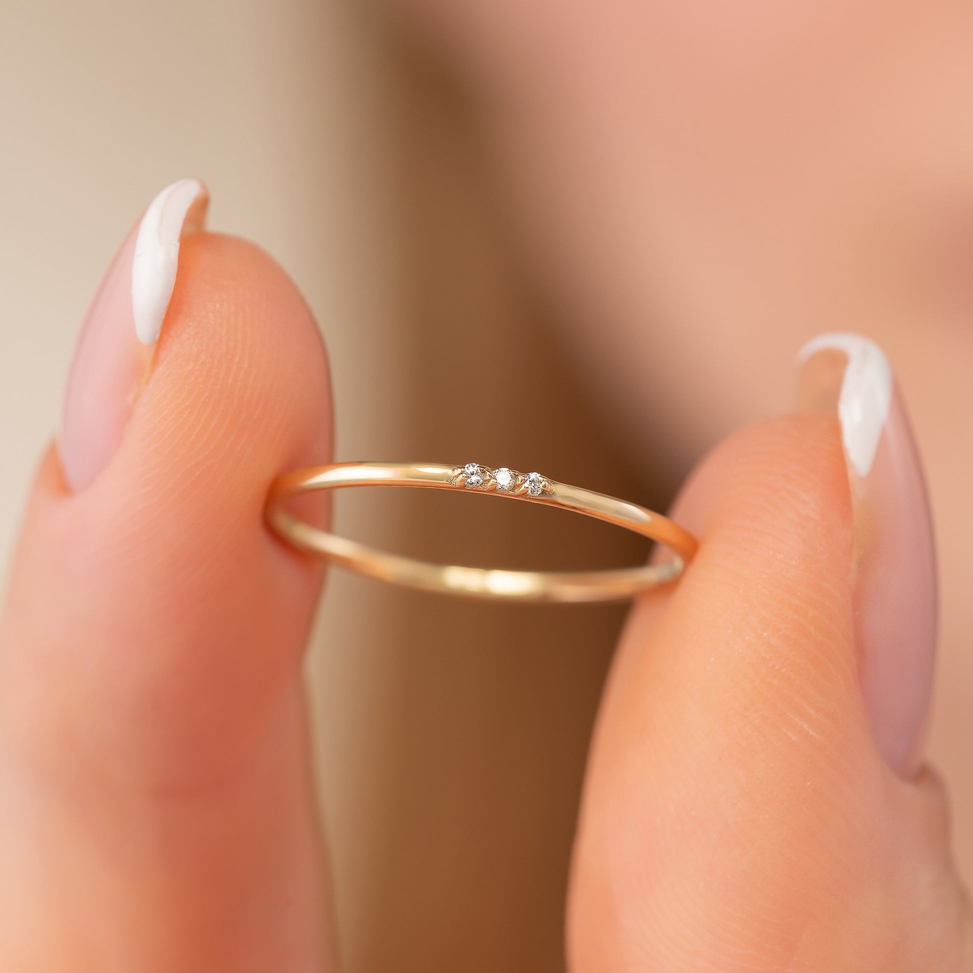 A close-up image of a person's fingers holding a delicate gold ring with a small gemstone.