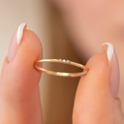 A close-up image of a person's fingers holding a delicate gold ring with a small gemstone.