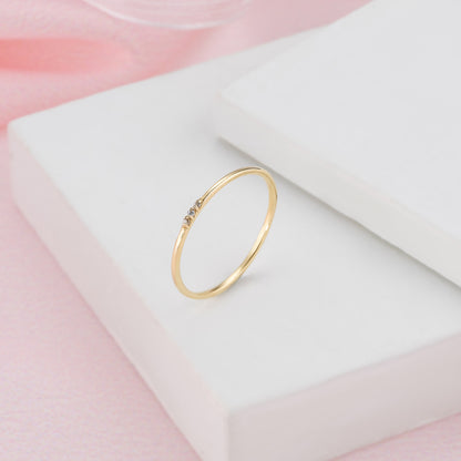 A delicate gold ring with a small gemstone is displayed on a white surface against a pink background.