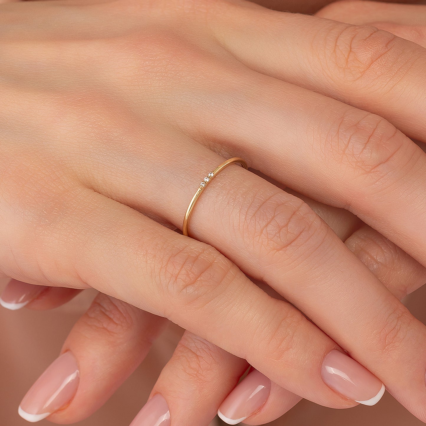 A close-up image of a person's hand wearing a gold ring with a small diamond.