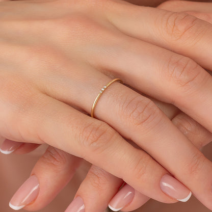 A close-up image of a person's hand wearing a gold ring with a small diamond.