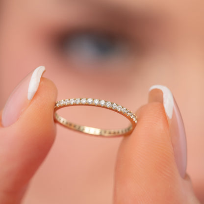 A close-up of a person's hand holding a gold ring with a row of small diamonds on it.