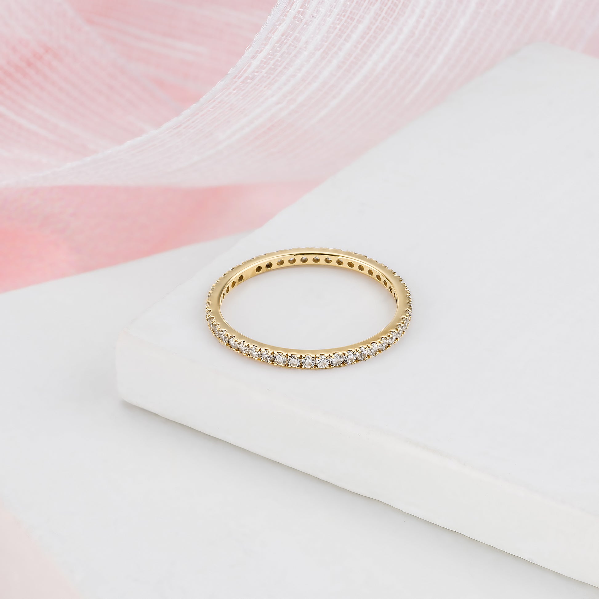A gold band ring with small diamonds set in it, resting on a white surface.