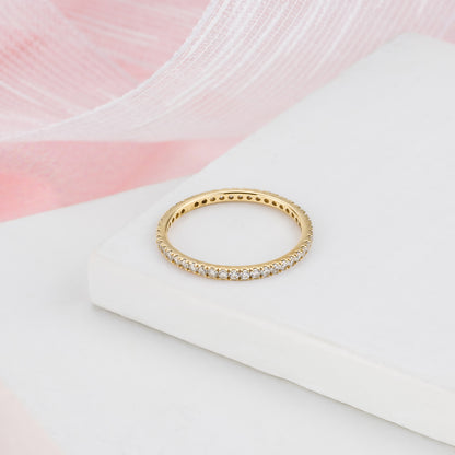 A gold band ring with small diamonds set in it, resting on a white surface.