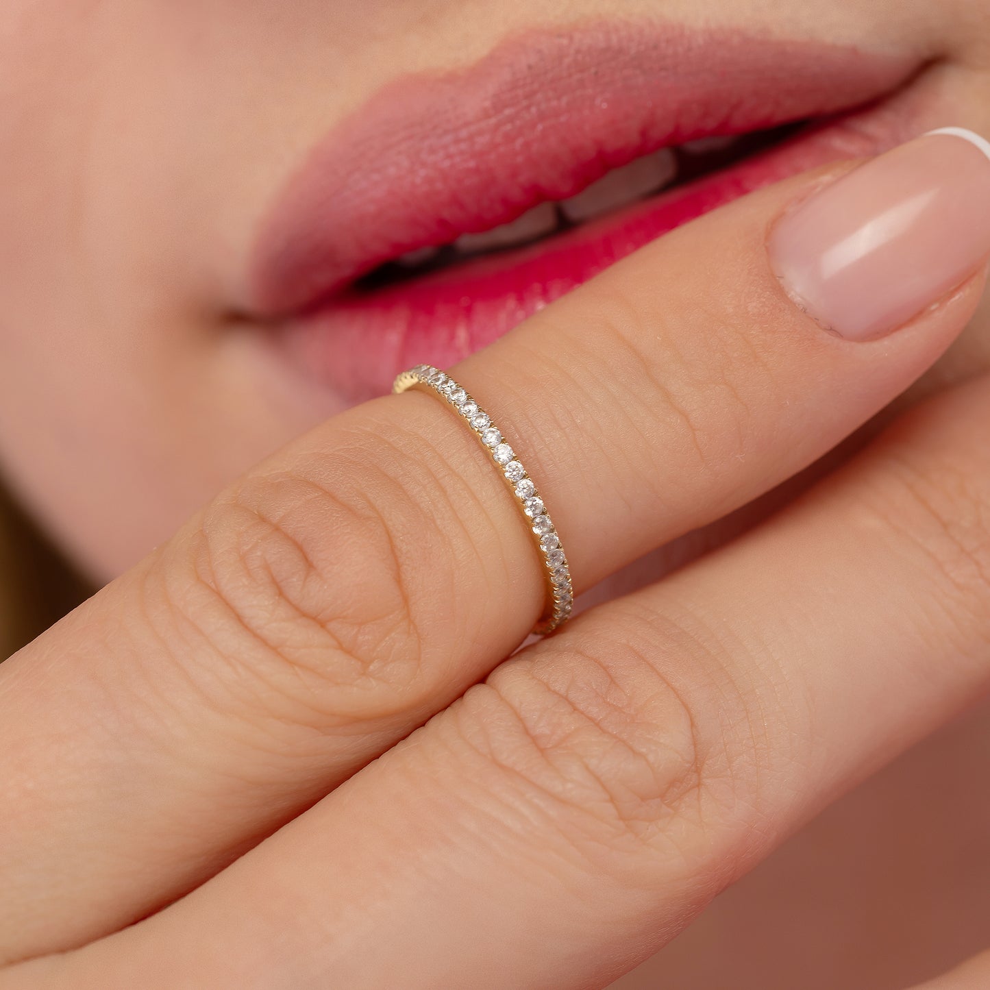 A close-up of a person's hand wearing a delicate gold ring with a row of small diamonds.