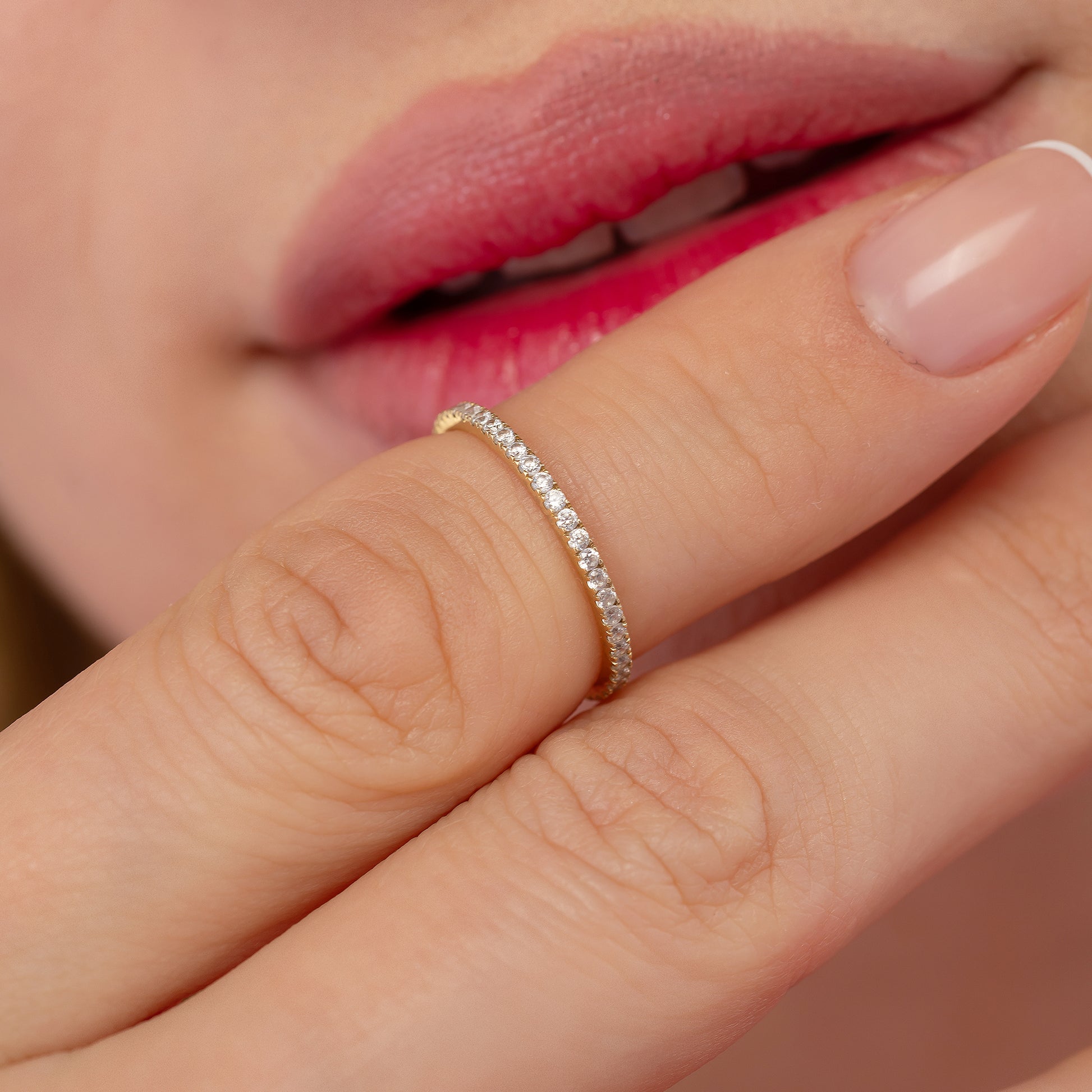 A close-up of a person's hand wearing a delicate gold ring with a row of small diamonds.