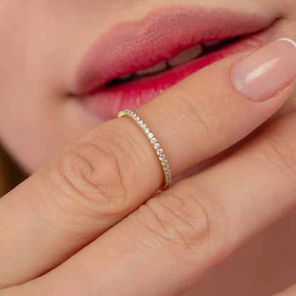 A close-up of a person's hand wearing a delicate gold ring with a row of small diamonds.