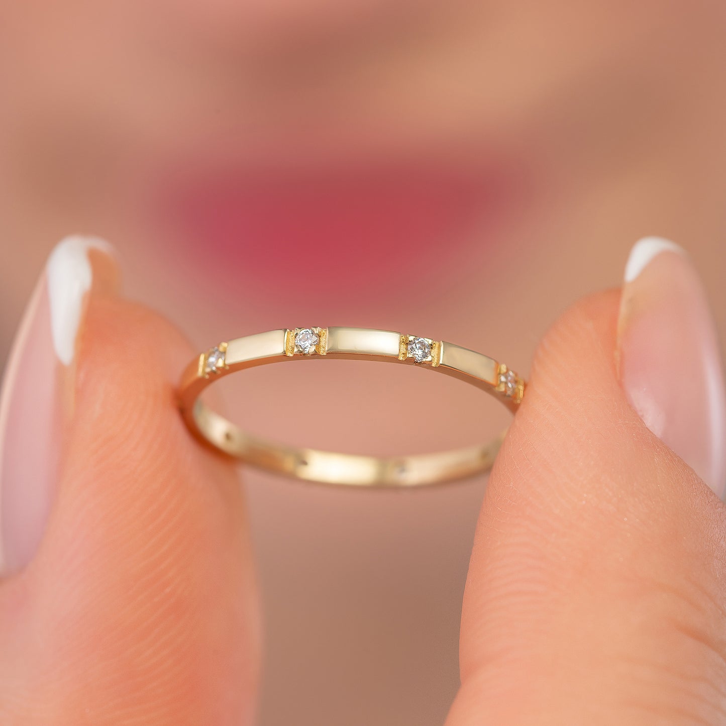 A close-up image of a person's fingers holding a gold ring with small diamonds.