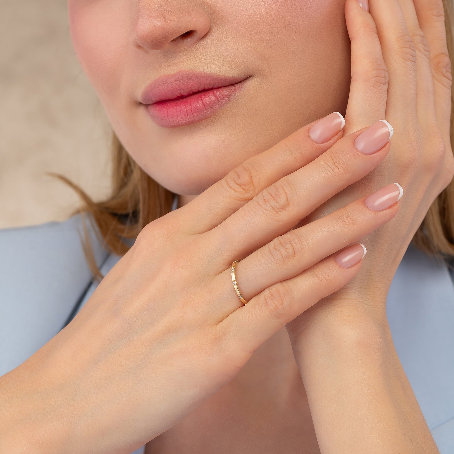 A close-up of a woman's face, focusing on her hands and fingers. She is wearing a gold ring on her finger.