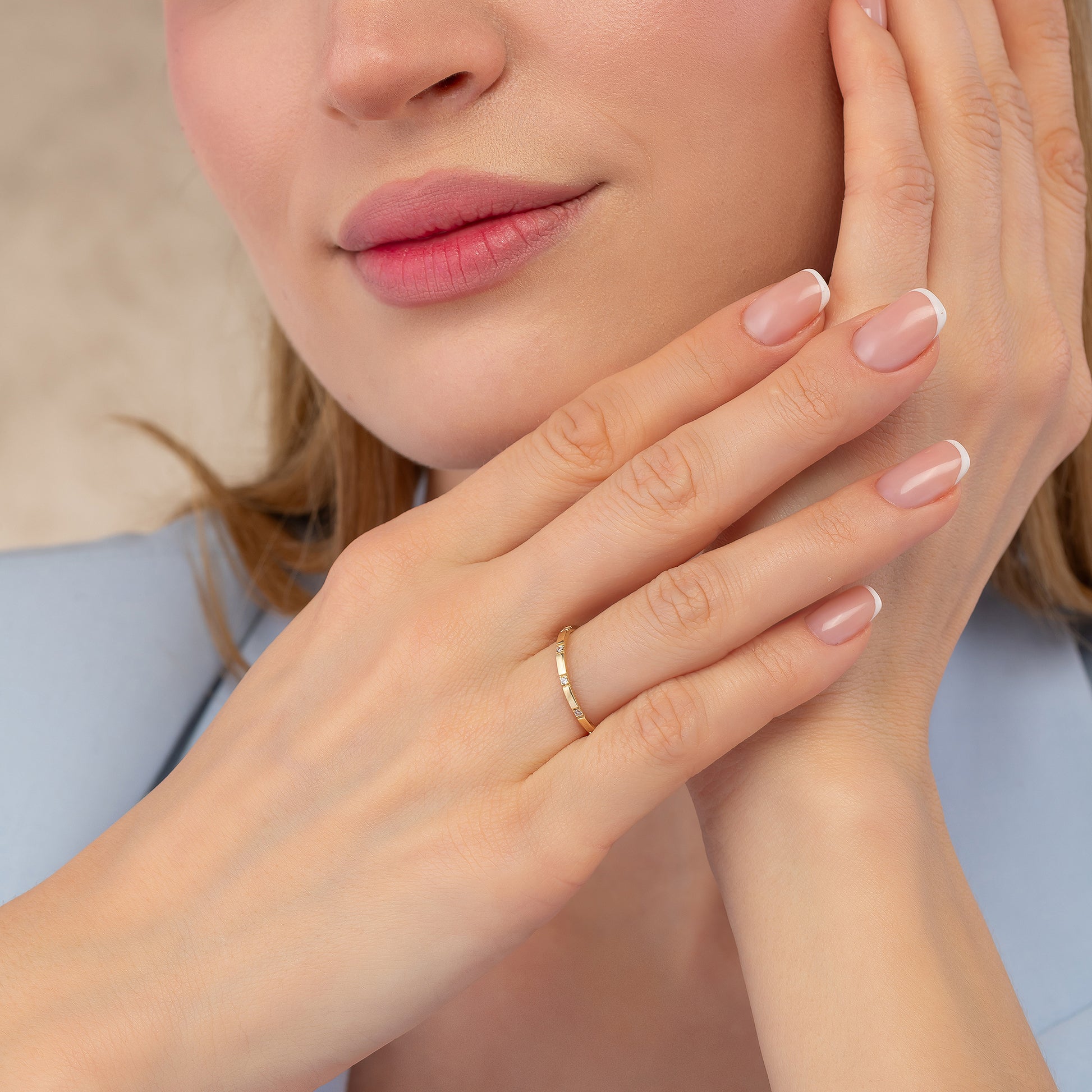 A close-up of a woman's face, focusing on her hands and fingers. She is wearing a gold ring on her finger.