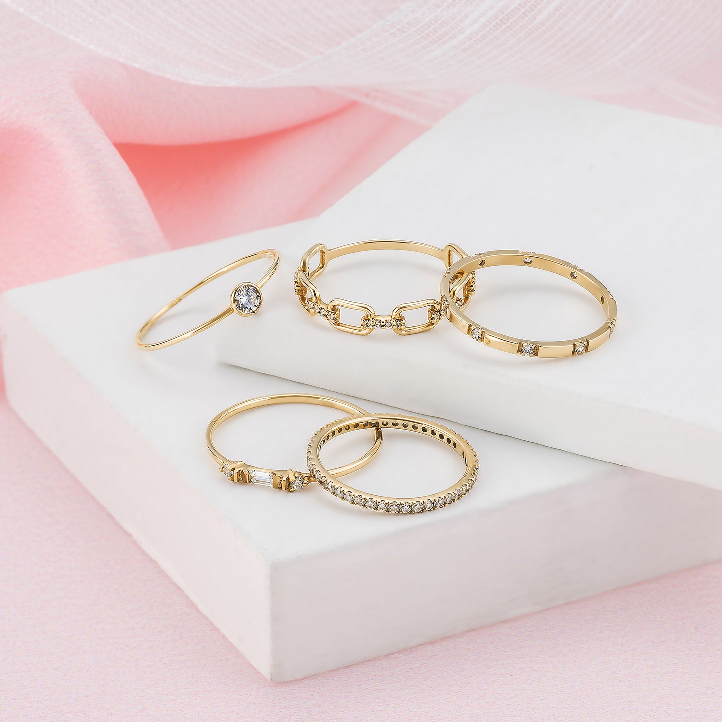 A collection of gold rings with various designs, including a ring with a large gemstone, displayed on a white surface against a pink background.
