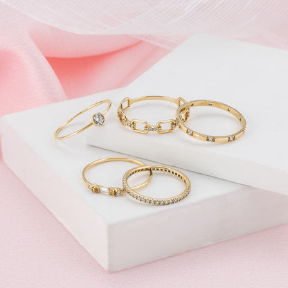 A collection of gold rings with various designs, including a ring with a large gemstone, displayed on a white surface against a pink background.
