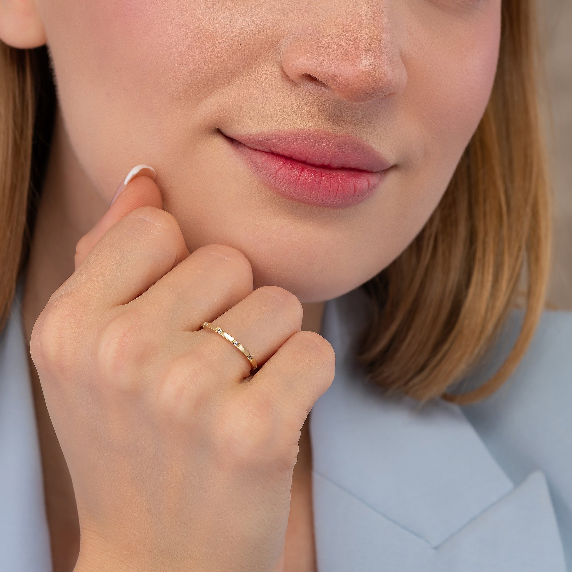A close-up of a woman's face, focusing on her hand and finger adorned with a ring.