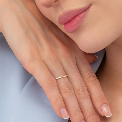 A close-up image of a person's hand wearing a gold ring, with their lips and chin visible.