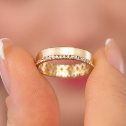 A close-up image of a person's fingers holding a gold ring with a row of small diamonds along the band.