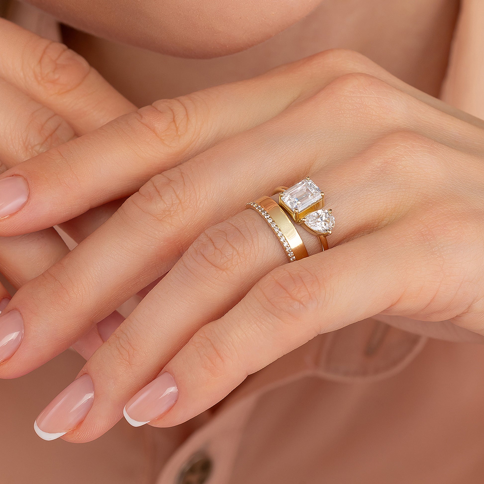 A close-up of a person's hand wearing a gold ring with a large diamond and a smaller diamond on top of it.