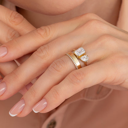 A close-up of a person's hand wearing a gold ring with a large diamond and a smaller diamond on top of it.